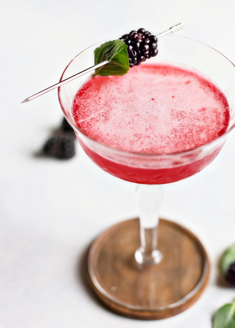 close up of blackberry simple syrup in a cocktail glass with fresh blackberries and basil