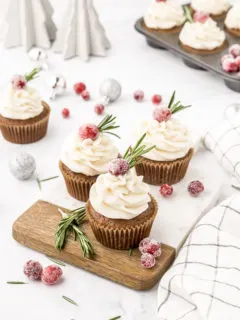 gingerbread cupcakes with cream cheese frosting on them arranged on a cutting board with cranberry garnish