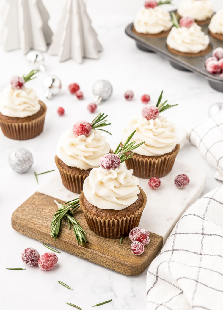 gingerbread cupcakes with cream cheese frosting on them arranged on a cutting board with cranberry garnish