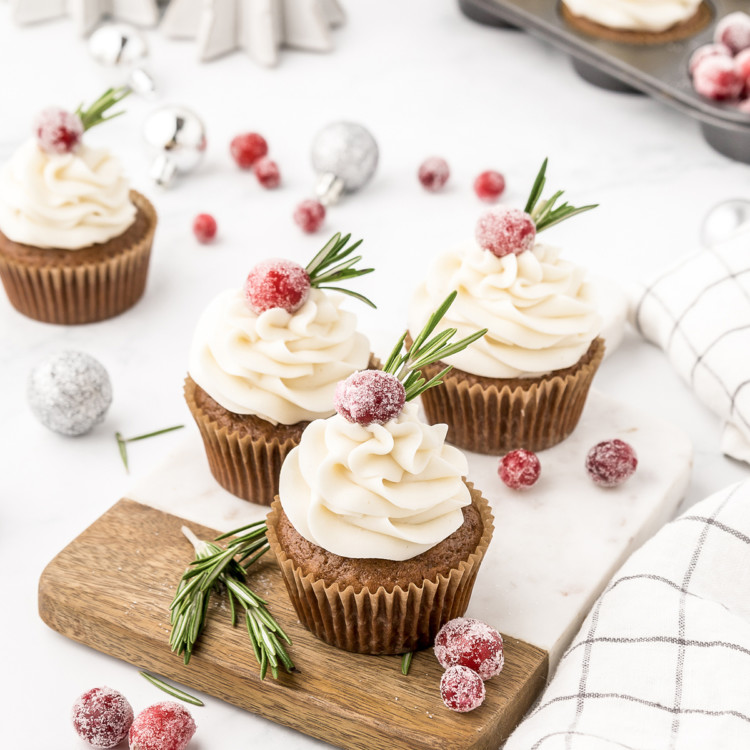 gingerbread cupcakes with cream cheese frosting on them arranged on a cutting board with cranberry garnish