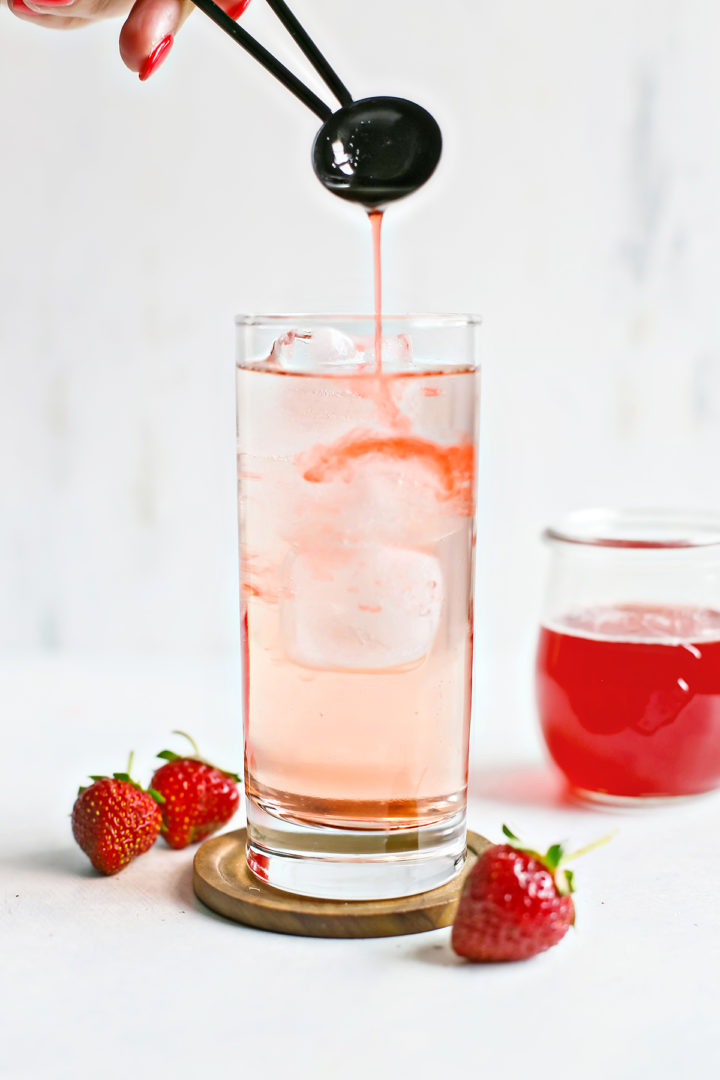 woman adding strawberry simple syrup to a glass with ice and liquid