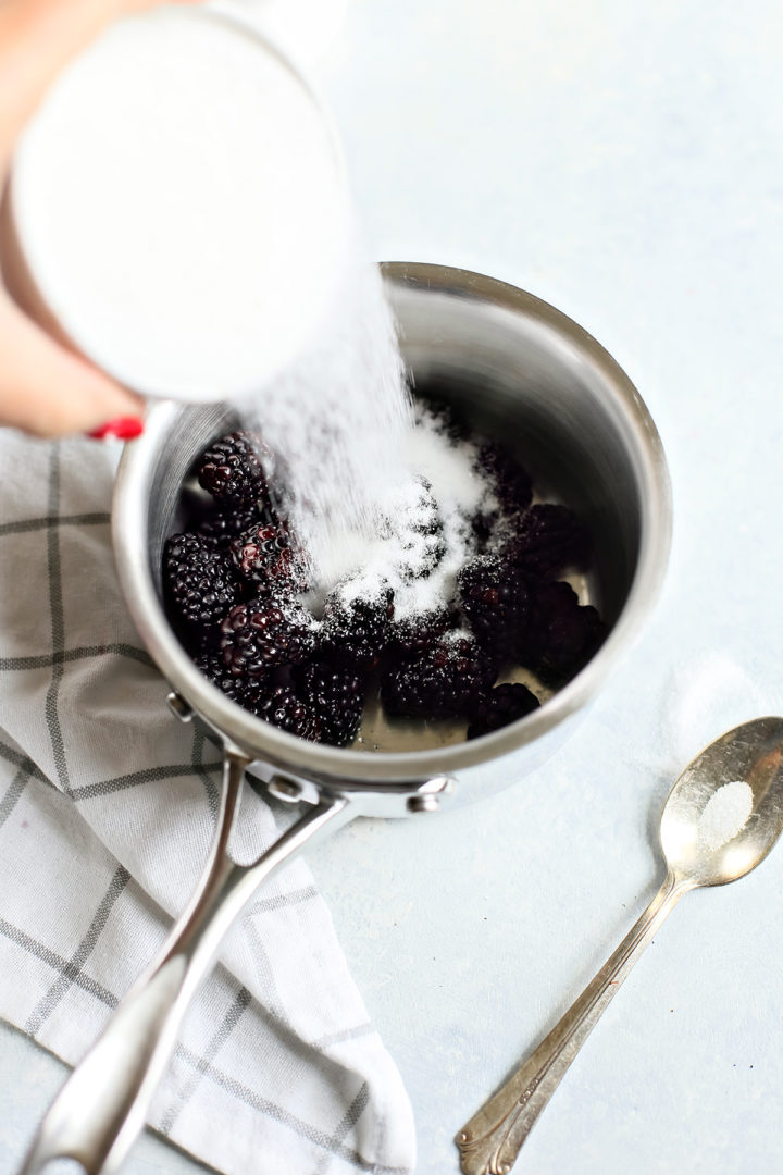 woman adding sugar to a pot of blackberries to make blackberry syrup for cocktails