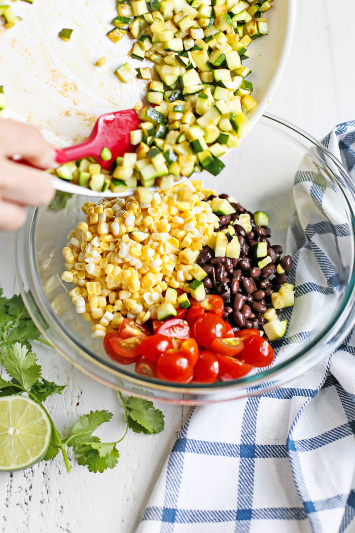 woman adding cooked zucchini to a glass bowl with other ingredients for the zucchini salsa recipe