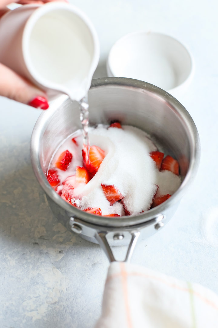adding sugar and water to a saucepan with fresh strawberries to make a recipe for strawberry simple syrup