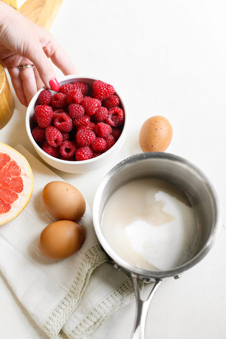 saucepan with sugar and grapefruit juice, woman picking up a bowl of fresh raspberries to make raspberry curd