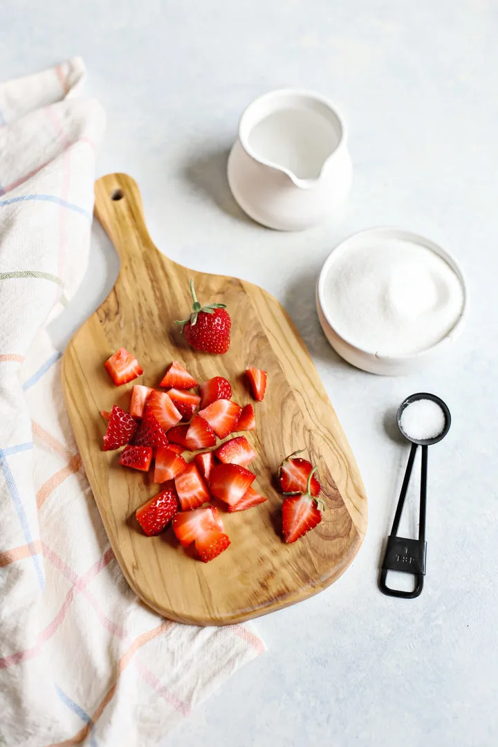 chopped strawberries on a wooden cutting board next to a bowl of sugar and water for making simple syrup with strawberries