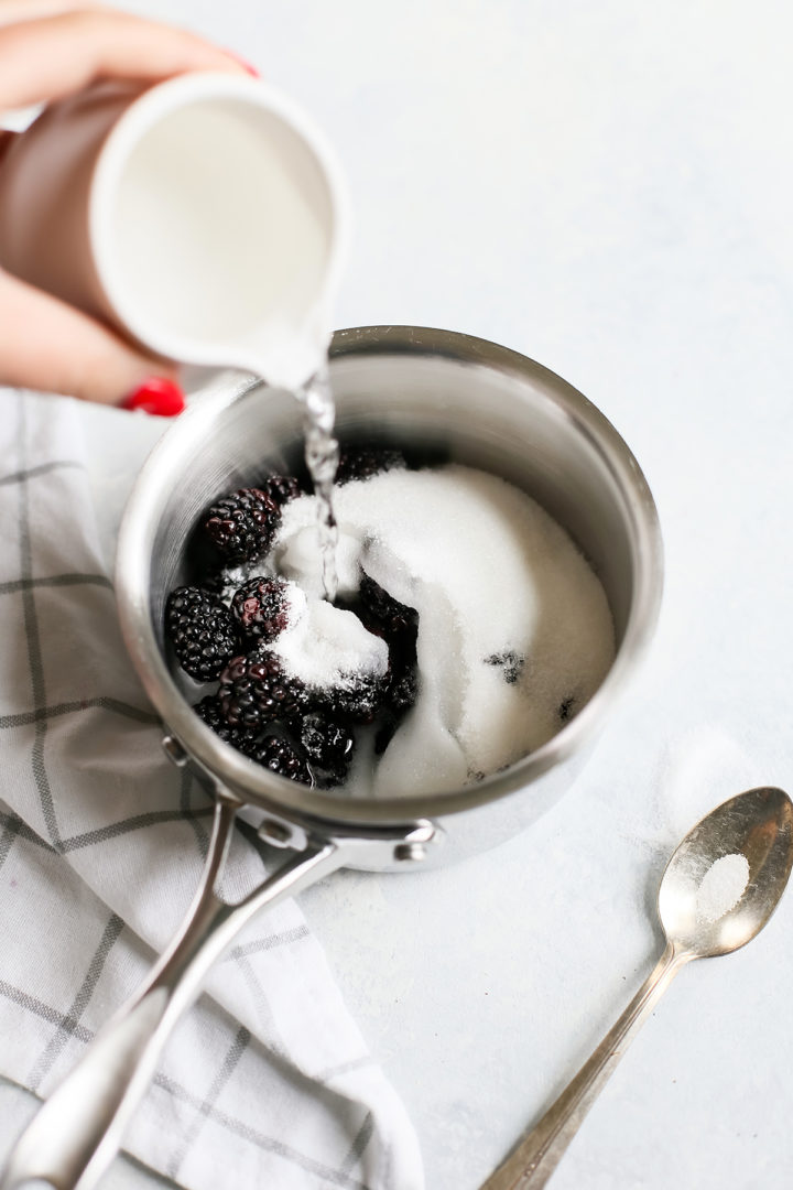 woman adding water to a pot with sugar and blackberries to make blackberry simple syrup