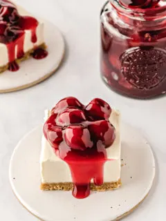 square slices of no bake cheesecake bars topped with cherry pie filling on white plates