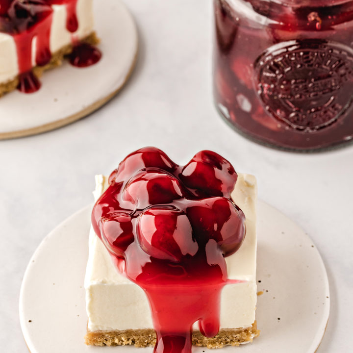 square slices of no bake cheesecake bars topped with cherry pie filling on white plates