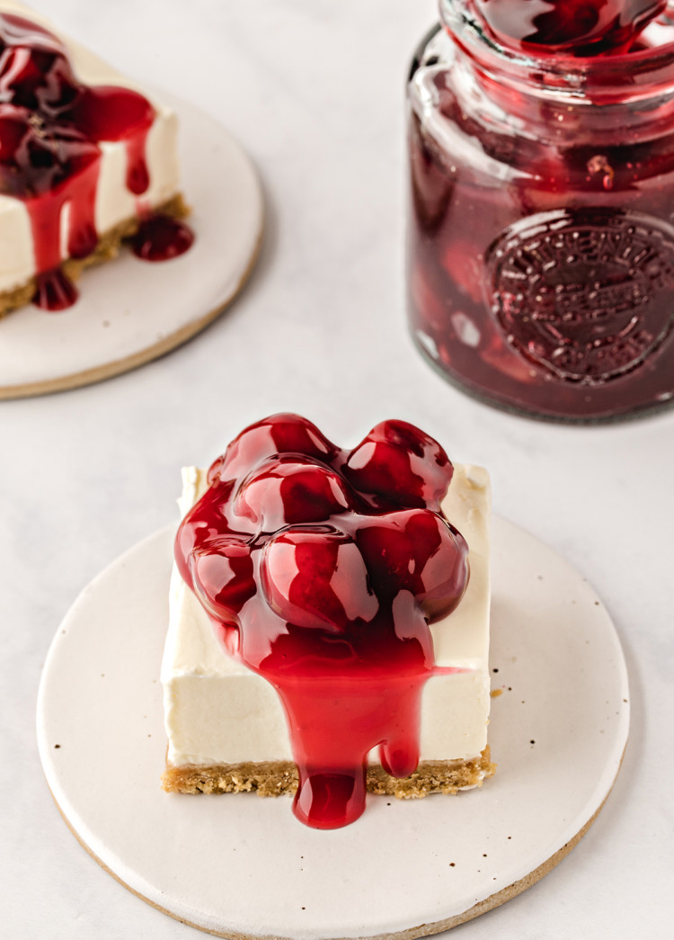 square slices of no bake cheesecake bars topped with cherry pie filling on white plates