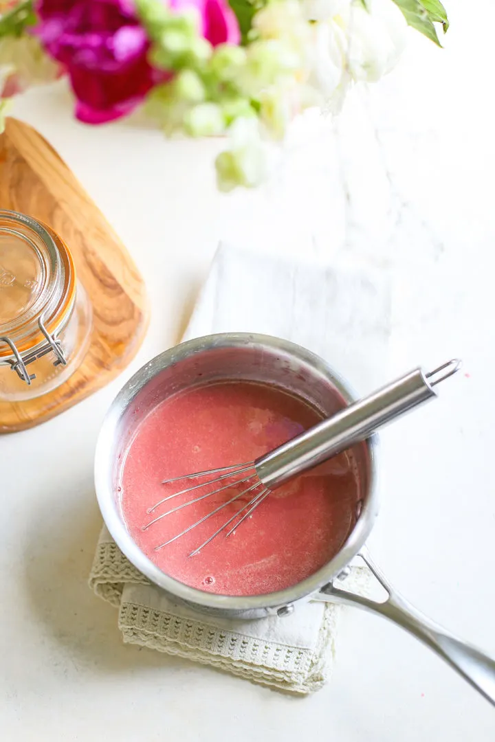 saucepan of prepared raspberry curd with a whisk in it 