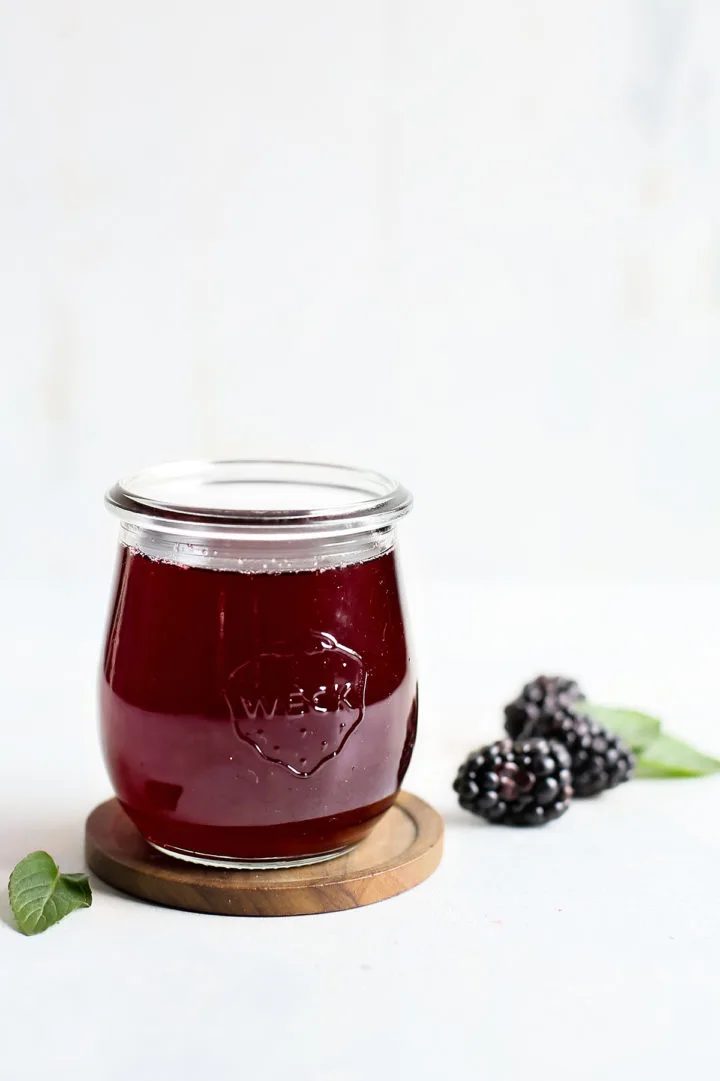 a jar of homemade blackberry simple syrup on a white background with fresh blackberries