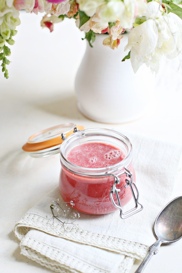 jar of raspberry curd on a white counter with a vase of flowers