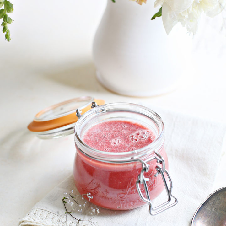 a jar of raspberry curd on a white counter with a vase of flowers
