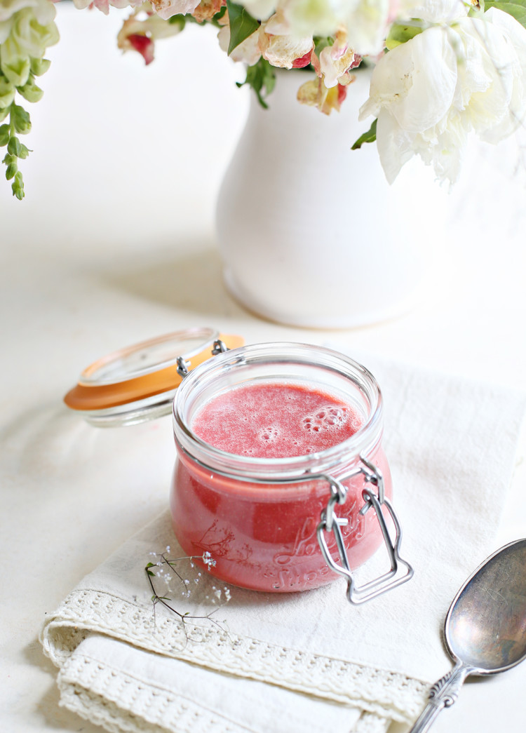a jar of raspberry curd on a white counter with a vase of flowers