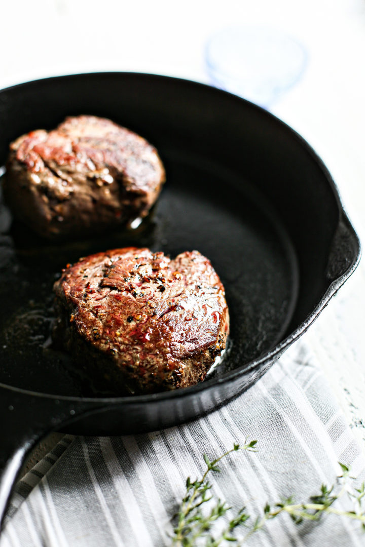 steaks cooking in a cast iron pan to serve with gremolata