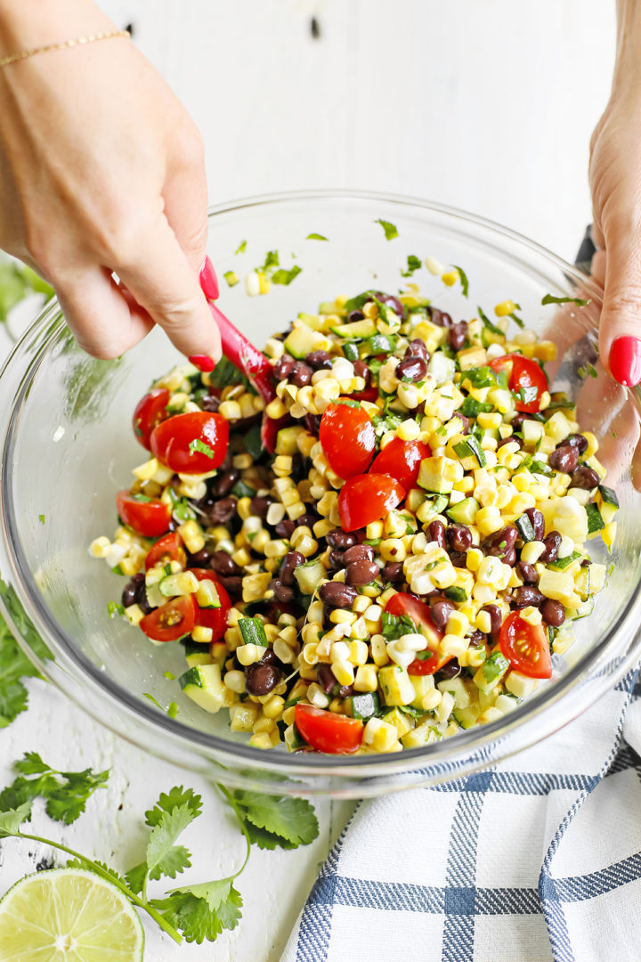 woman stirring ingredients in zucchini salsa in a glass bowl