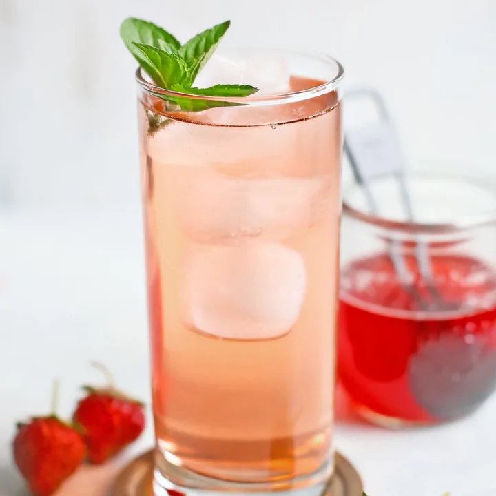 drink made with strawberry simple syrup served in a tall clear glass with a mint garnish