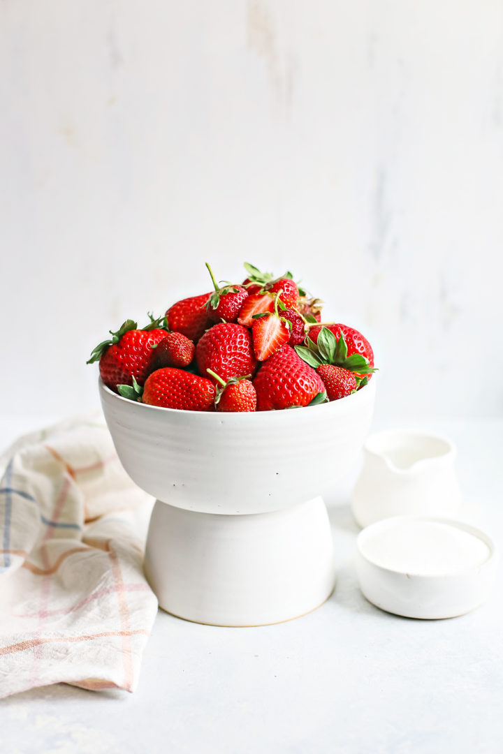 fresh strawberries, water, and sugar in white bowls to make strawberry simple syrup