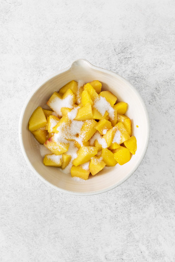 cut peaches in a bowl with sugar to prepare for freezing