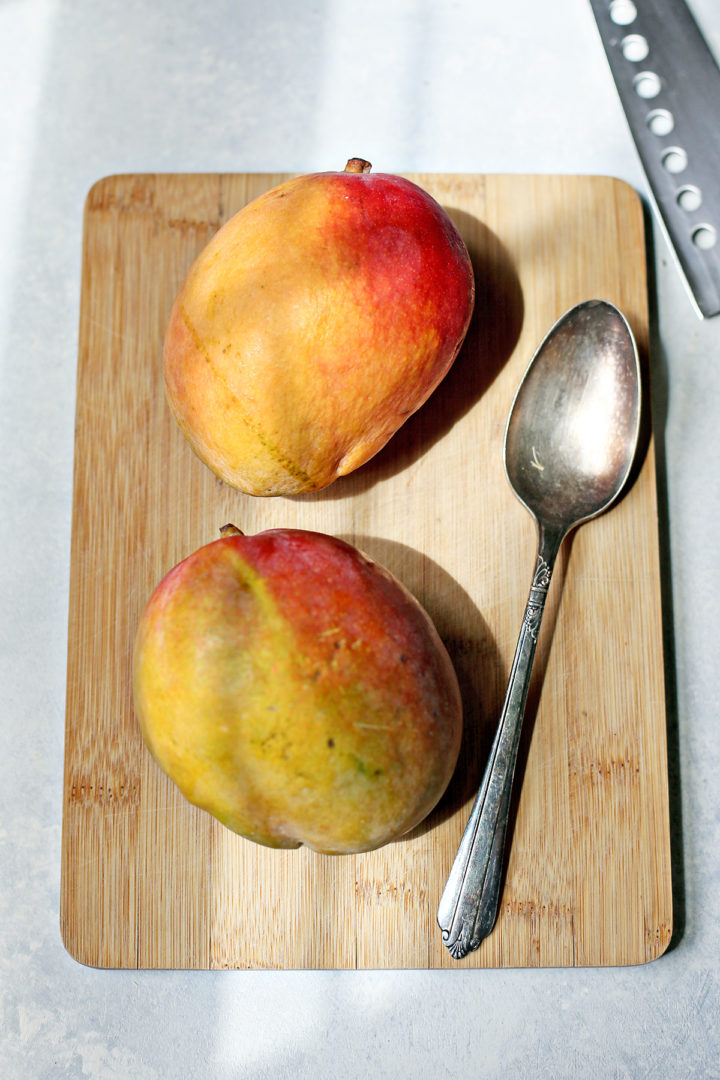 a mango cut in half on a cutting board