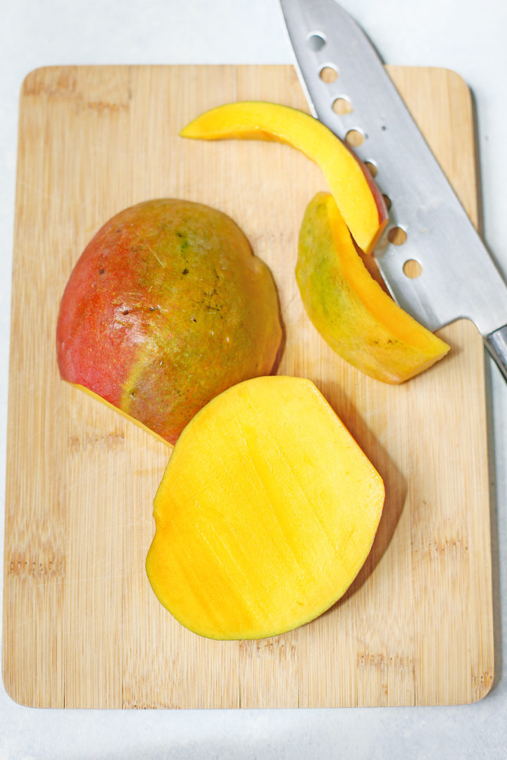 a cut mango on a wooden cutting board with a knife