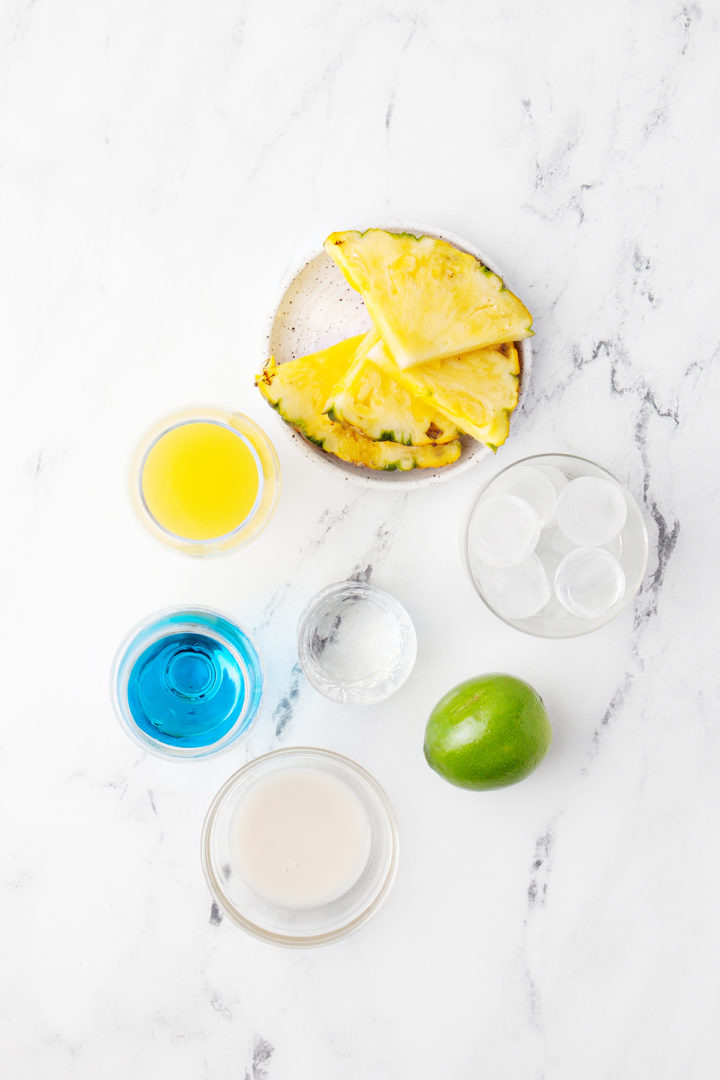 ingredients needed to make a blue hawaiian drink on a marble counter