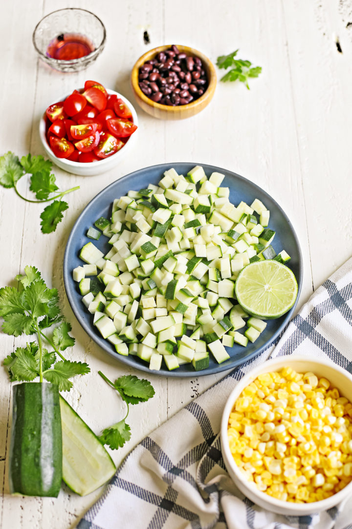 ingredients needed to make zucchini salsa arranged on a white wooden table