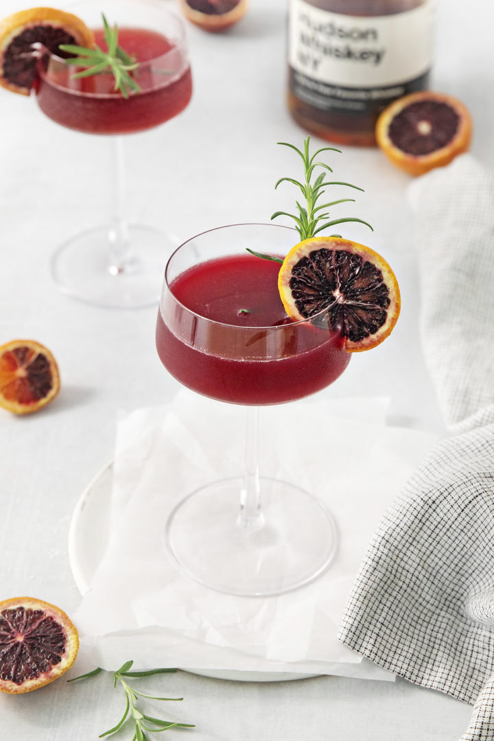 blood orange whiskey sour served in a coupe glass with rosemary and orange garnish