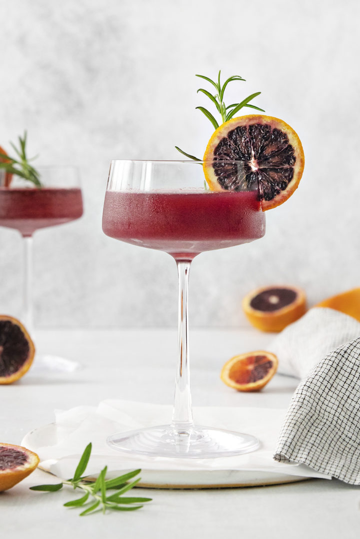 close up photo of a blood orange whiskey sour in a coupe glass on a light background