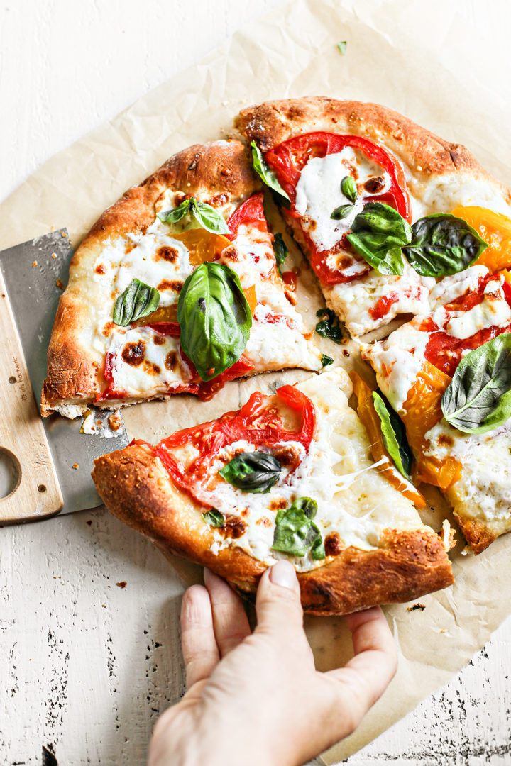 homemade caprese pizza cut into four slices on top of a sheet of parchment paper