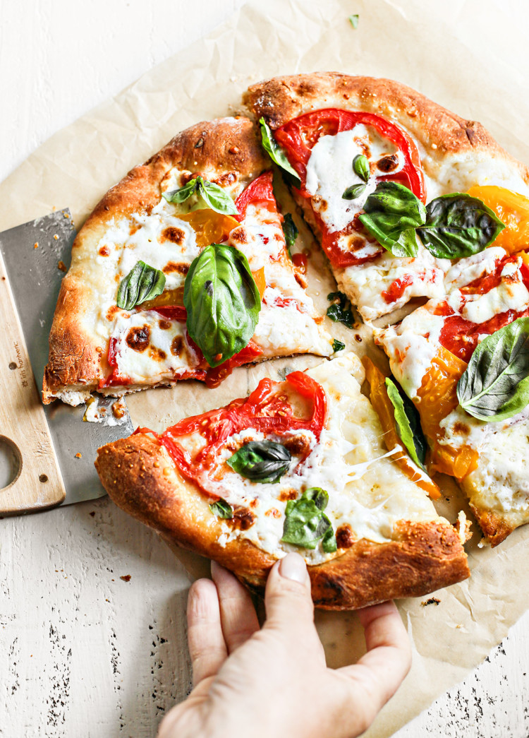 woman picking up a slice of caprese pizza