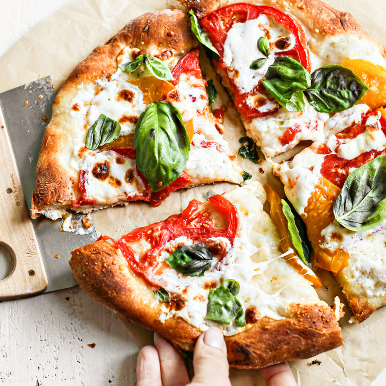 woman picking up a slice of caprese pizza