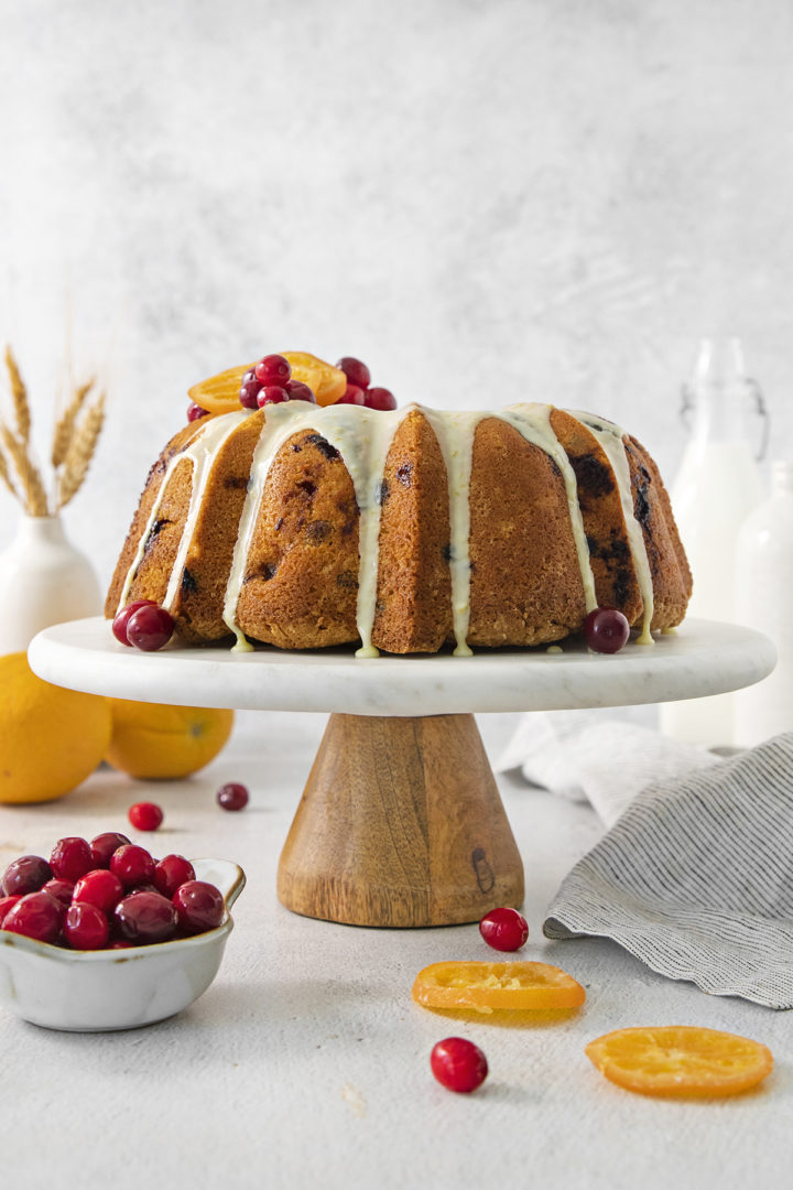 cranberry orange cake with orange glaze on a wood and marble cake stand