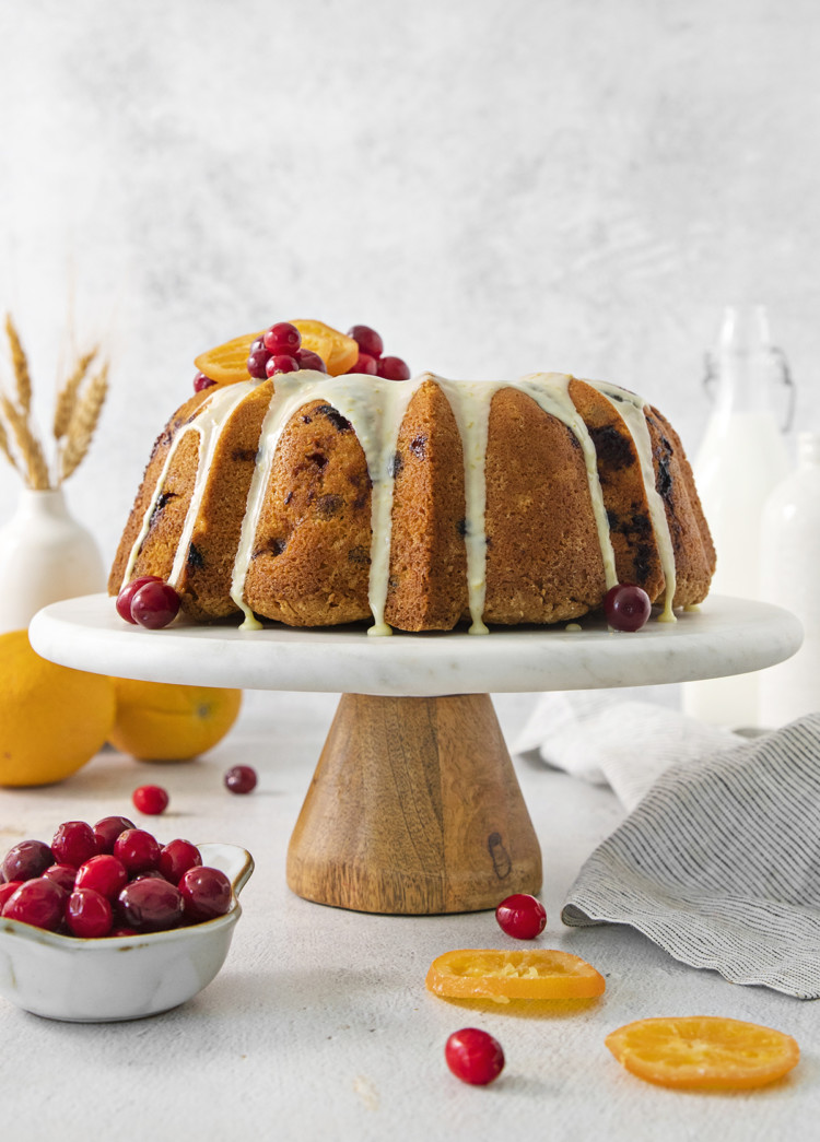 cranberry orange cake on a cake stand surrounded by orange slices and fresh cranberries