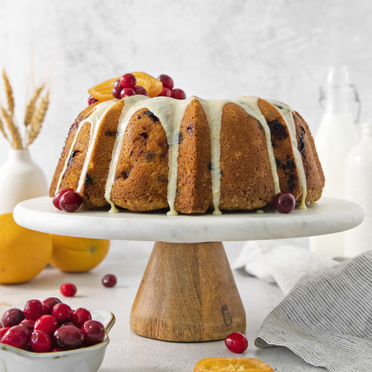 cranberry orange cake on a cake stand surrounded by orange slices and fresh cranberries