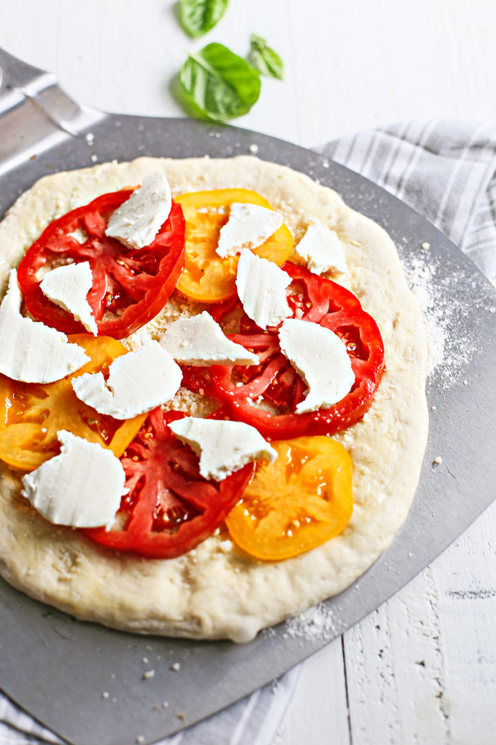 showing assembly of caprese pizza - adding mozzarella