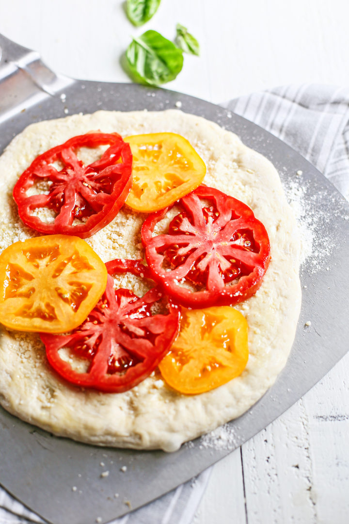 adding fresh tomatoes on the pizza dough to make caprese pizza