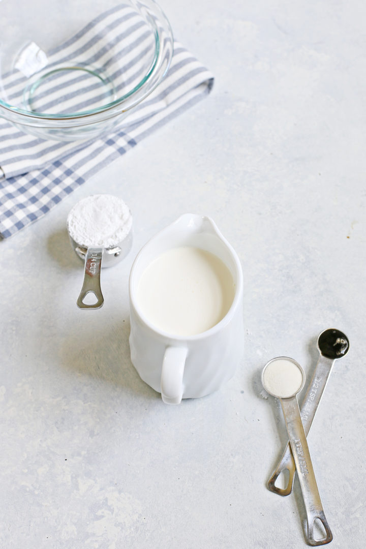 All ingredients for stabilized whipped cream—heavy cream, powdered sugar, gelatin, and vanilla—measured and arranged on a light surface.