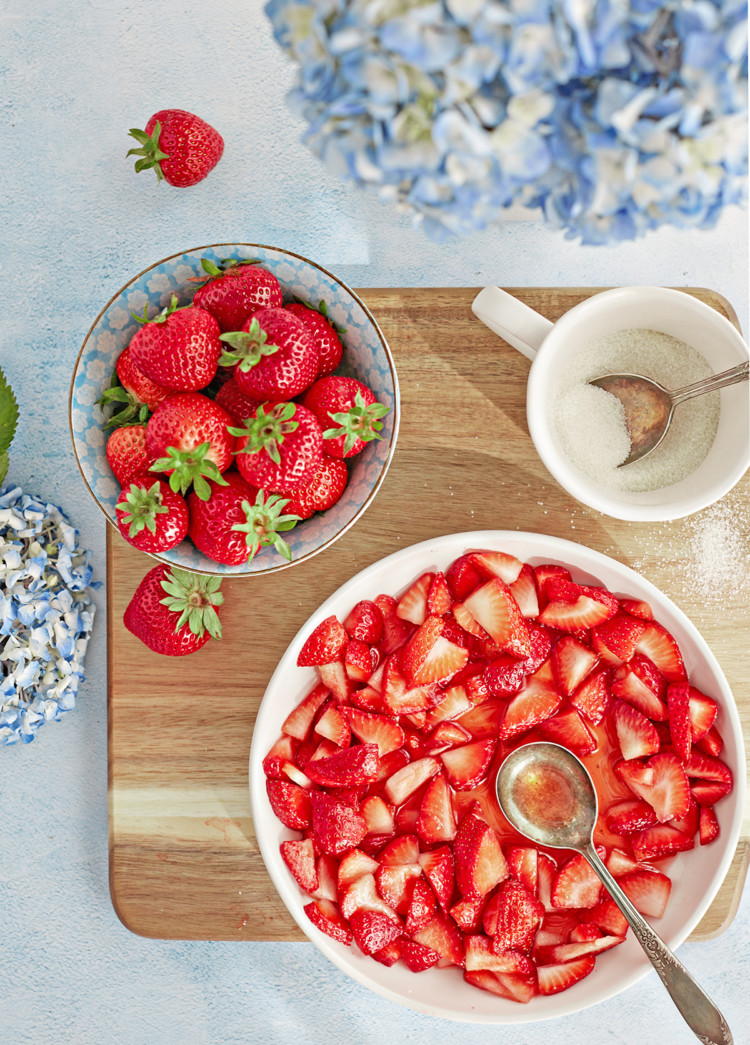 overhead photo of a bowl of macerated strawberries on a cutting board