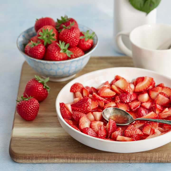 a white bowl of macerated strawberries on a wooden cutting board