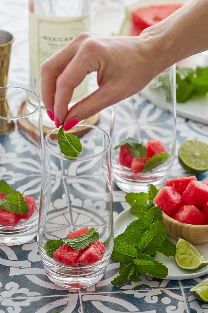 woman adding fresh mint leaves to a mojito glass with watermelon cubes