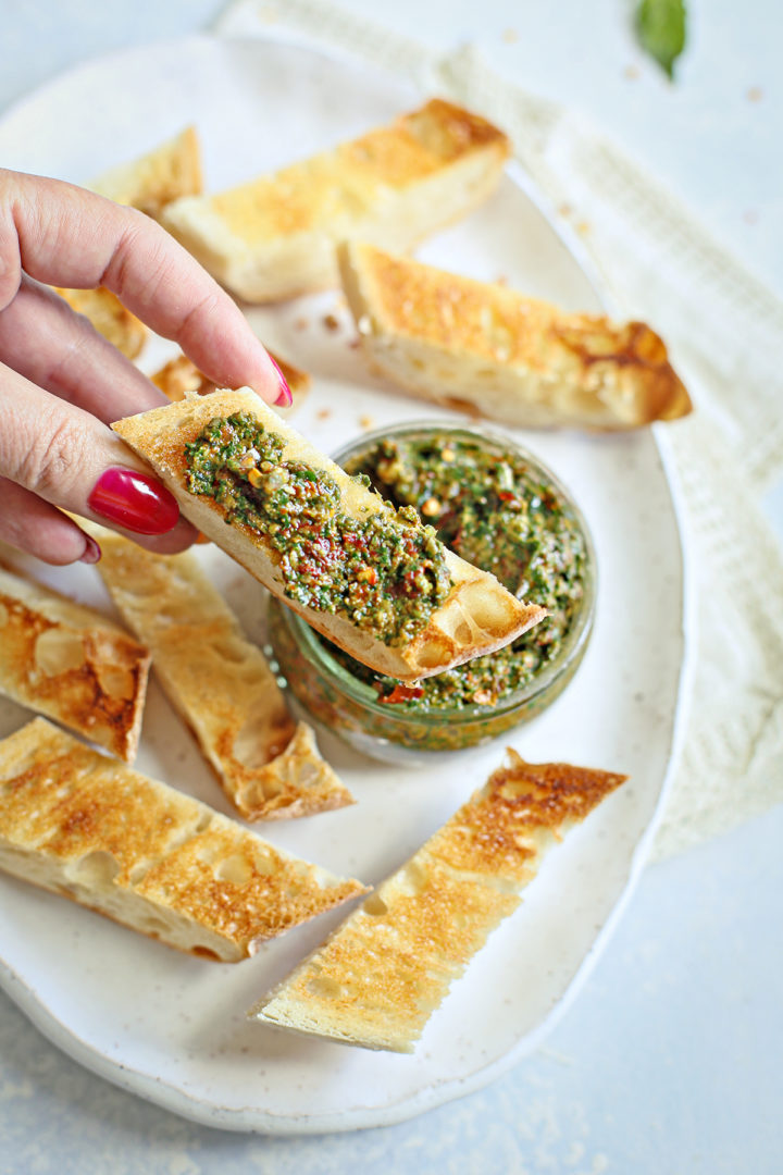 woman spreading sun dried tomato pesto on a piece of toasted baguette