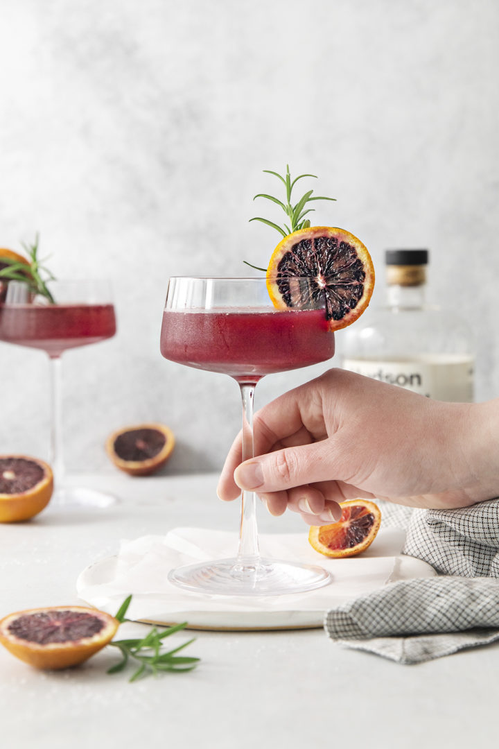 woman picking up a glass of blood orange whiskey sour