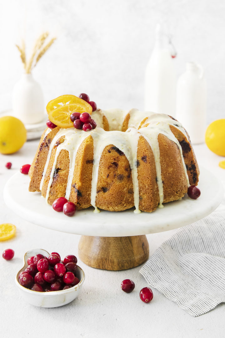 cranberry bundt cake on a cake stand garnished with cranberries and orange slices