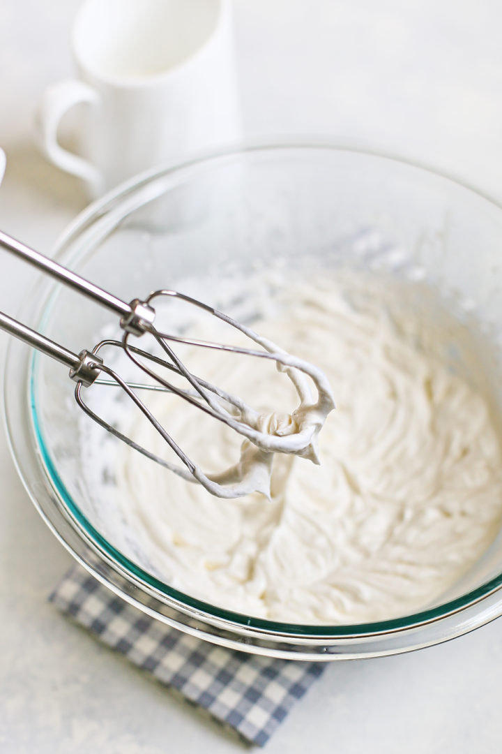 Beaters lifted from the bowl, holding stiff peaks of whipped cream—an indicator that the cream is properly whipped and stabilized.