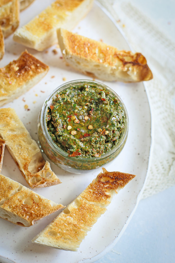 a jar of sun dried tomato pesto being served with toasted baguette