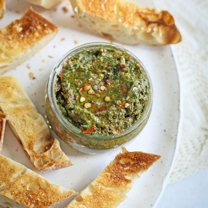 sun dried tomato pesto in a jar on a serving plate with toasted baguette