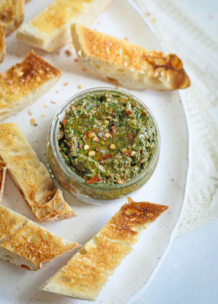 sun dried tomato pesto in a jar on a serving plate with toasted baguette