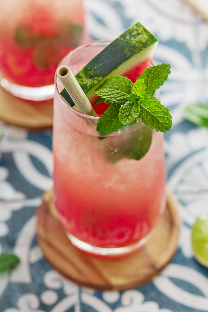 close up of a watermelon mojito in a glass garnished with fresh watermelon and mint